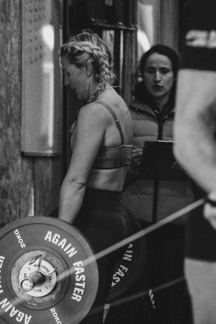 Female athlete lifting barbell supported by trainer
